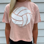 Woman wearing a peach t-shirt with a white volleyball graphic in front of a white wall