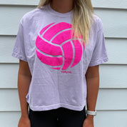 Person wearing a light purple t-shirt with a pink logo in front of a white wall.