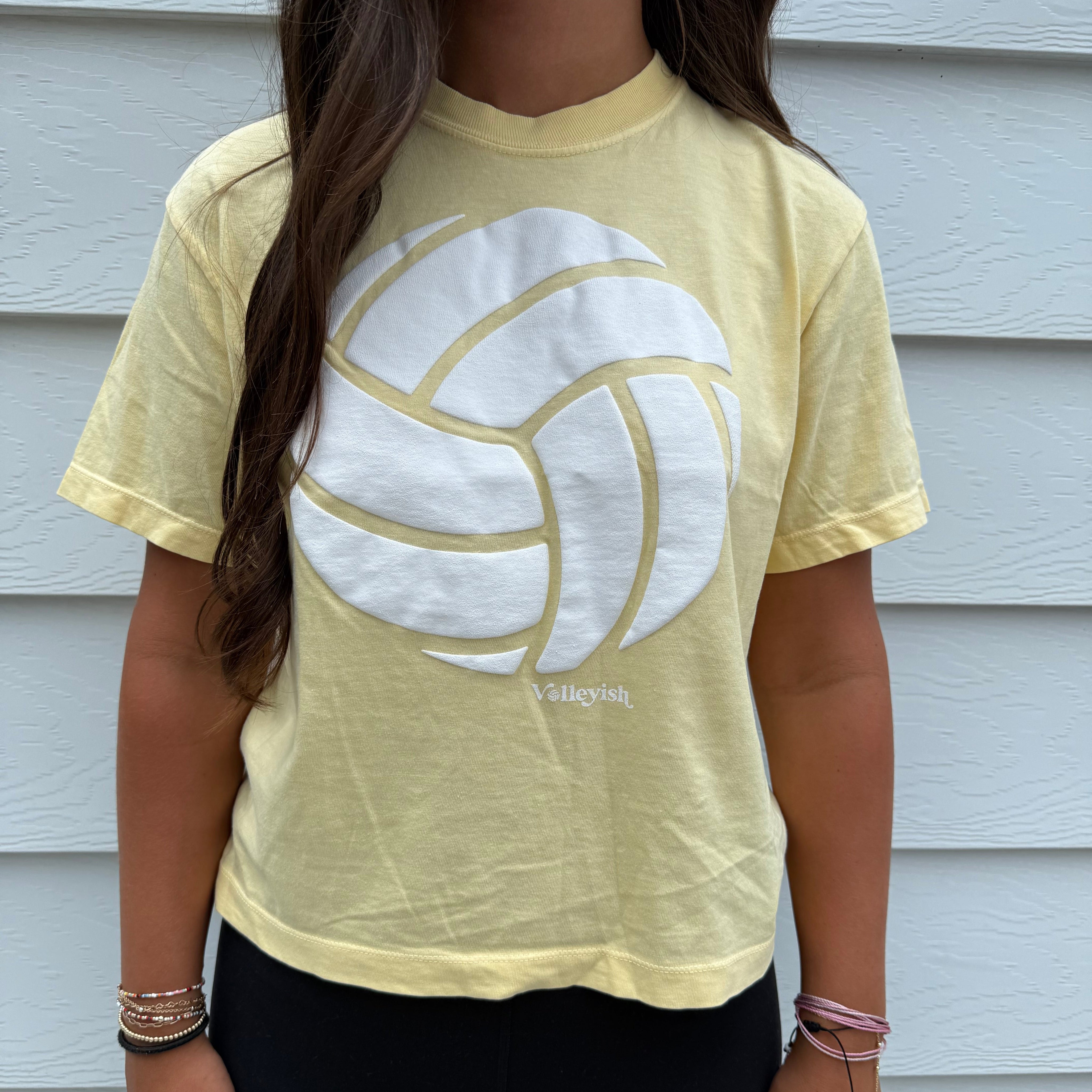 Woman wearing a yellow volleyball t-shirt with a white logo on a light background